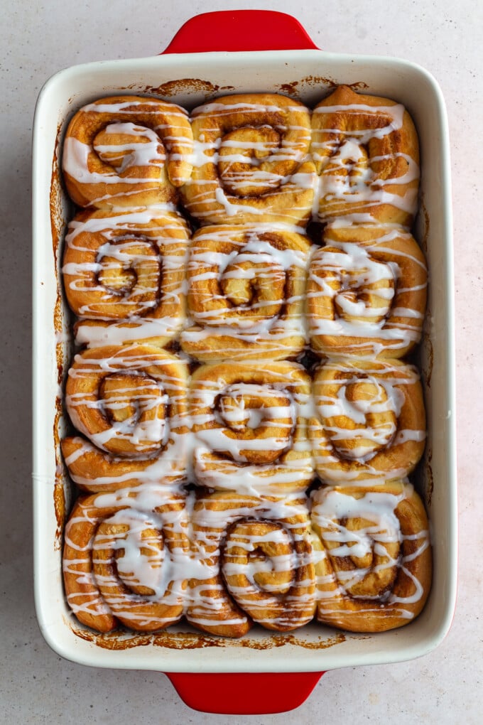 cinnamon rolls in a red pan that are drizzled with frosting