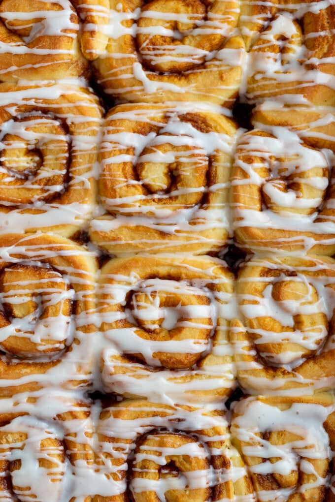 up close shot of cinnamon rolls in a pan that are drizzled with frosting