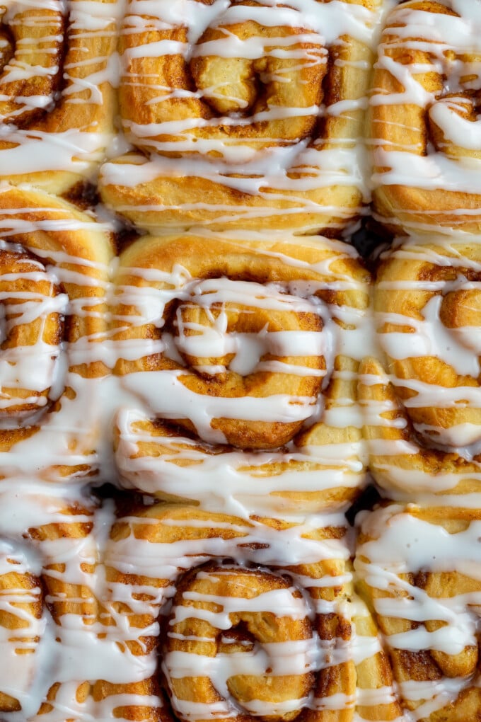 up close shot of cinnamon rolls in a pan that are drizzled with frosting