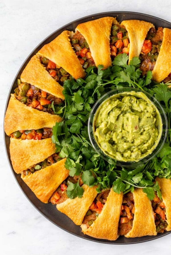 taco ring made out of crescent rolls in a circle and filled with beans and veggies. guacamole in the center of the ring