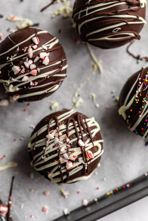 hot chocolate bombs topped with drizzled chocolate and sprinkles/ crushed peppermint all sitting on a baking sheet