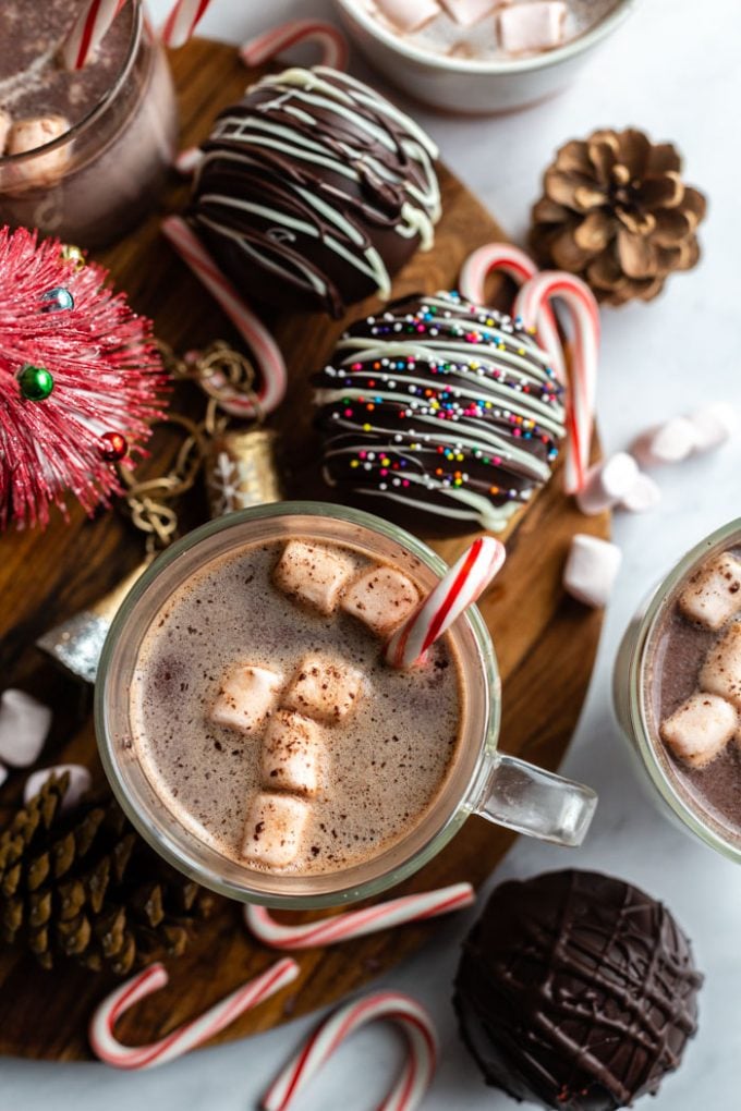 cup of hot chocolate with peppermint stick on the side and marshmallos floating on the top. several hot chocolate bombs around the glass