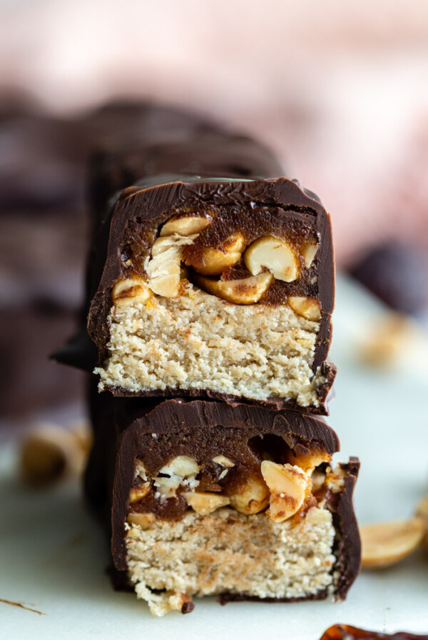 homemade snickers candy bar cut in half and stacked up so that you can see the inside of it. more bars in the background