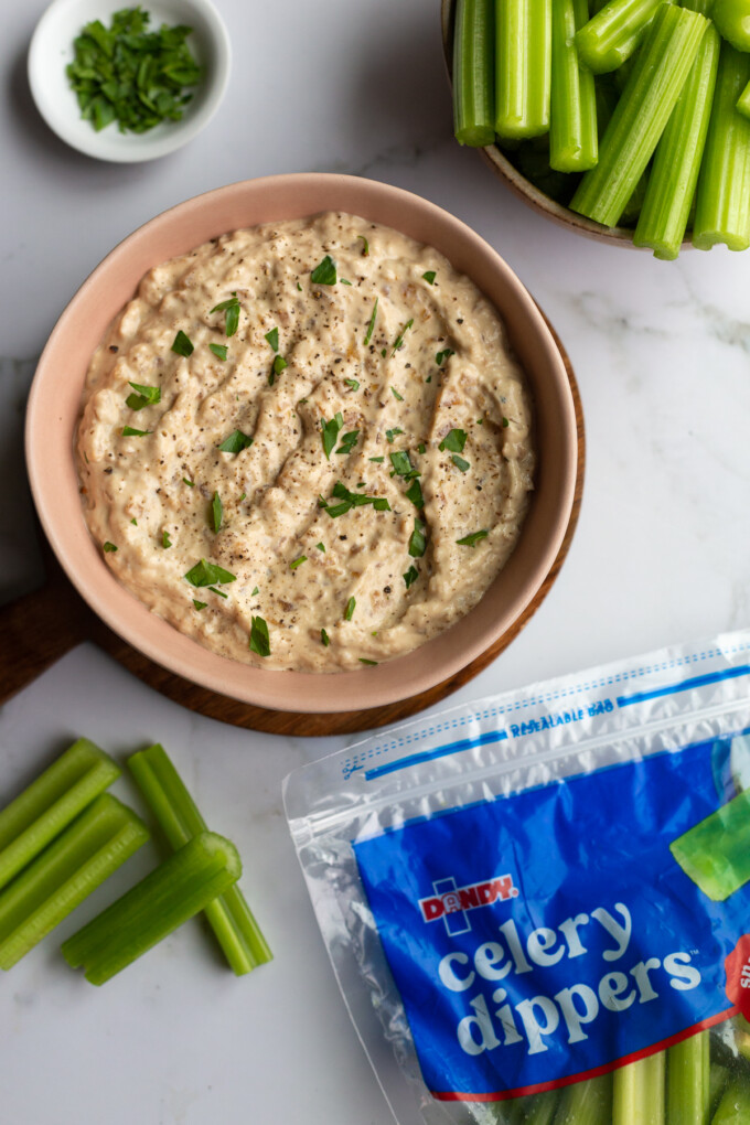 french onion dip in a pink bowl with a bag and bowl of celery in the corner of the shot