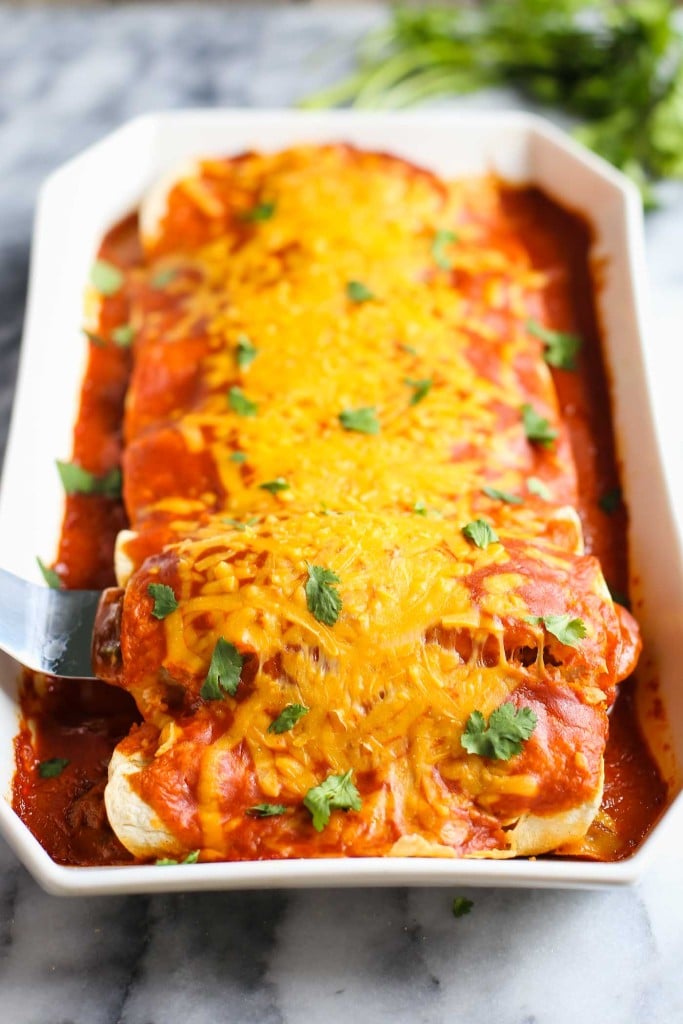 cheesy enchiladas in a casserole dish with one being scooped out