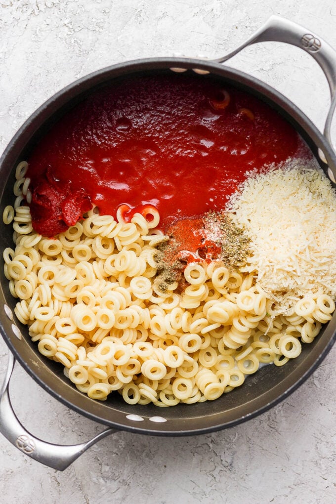 Combining pasta with tomato sauce and parmesan cheese in a large pot.