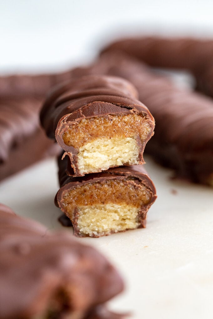 top down shot of homemade twix chocolate bars. There's extra chocolate drizzled on top of them in a swirled pattern. One or the bars is cut in half so that the can see the caramel and shortbread fiilling