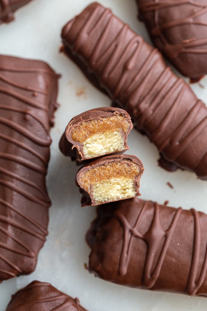 top down shot of homemade twix chocolate bars. There's extra chocolate drizzled on top of them in a swirled pattern. One or the bars is cut in half so that the can see the caramel and shortbread fiilling