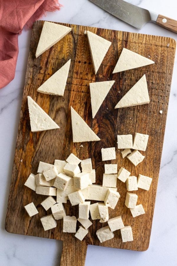 tofu on a cutting board with some cut into triangles and some is cut inot cubes