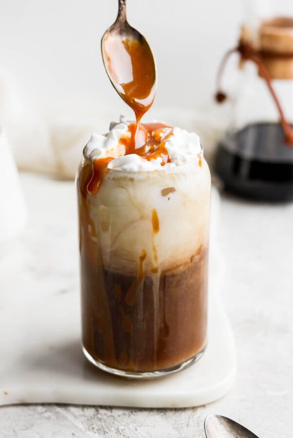 Using a spoon to drizzle caramel over the top of an iced latte.