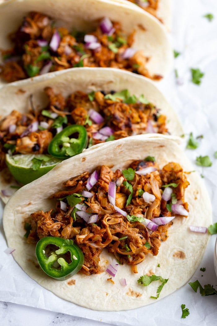 jackfruit carnitas tacos on flour tortillas and topped with onion, cilantro, and jalapeno