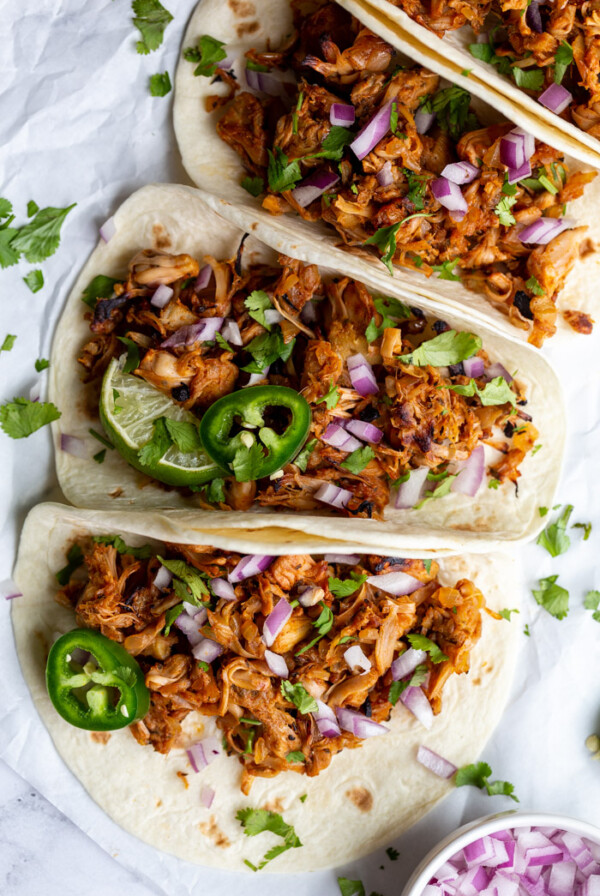 jackfruit carnitas tacos on flour tortillas and topped with onion, cilantro, and jalapeno