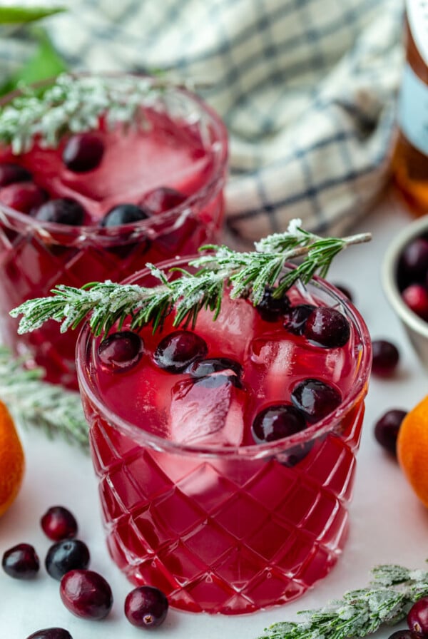 side shot of a cranberry whiskey cocktail with fresh cranberries in it and sugared rosemary sitting on the rim