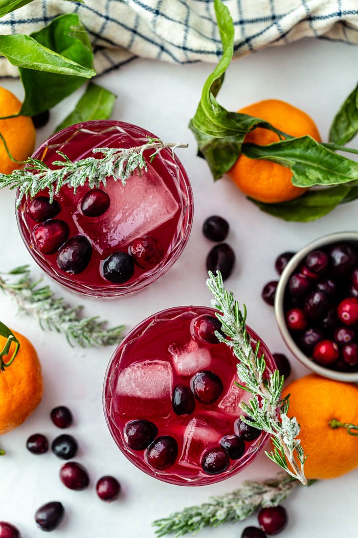 top down shot of a cranberry whiskey cocktail with fresh cranberries in it and sugared rosemary sitting on the rim