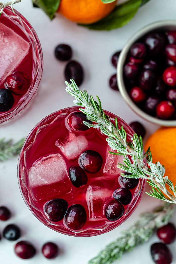 top down shot of a cranberry whiskey cocktail with fresh cranberries in it and sugared rosemary sitting on the rim