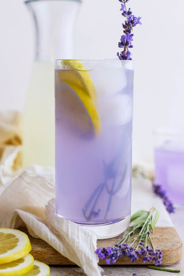 lavender lemonade in a tall glass with ice and fresh lavender plus lemon slices in the glass