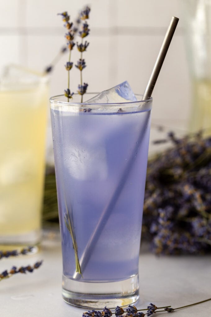 purple lavender lemonade in a tall glass with fresh lavender and a straw in it