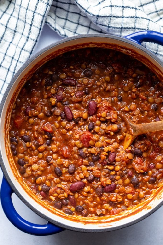 stirring lentil chili in a large pot with a wooden spoon