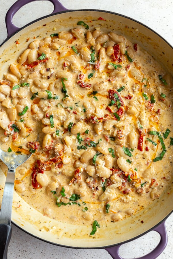 large skillet with creamy butter beans and sundried tomtoes in it known as "marry me butter beans". topped with fresh basil