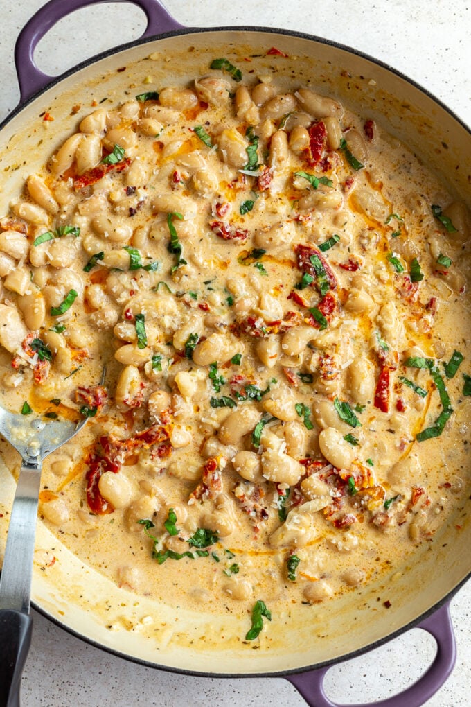 large skillet with creamy butter beans and sundried tomtoes in it known as "marry me butter beans". topped with fresh basil