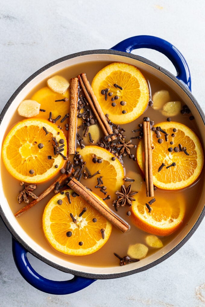 A drink with cinnamon sticks and orange slices in a large pot.