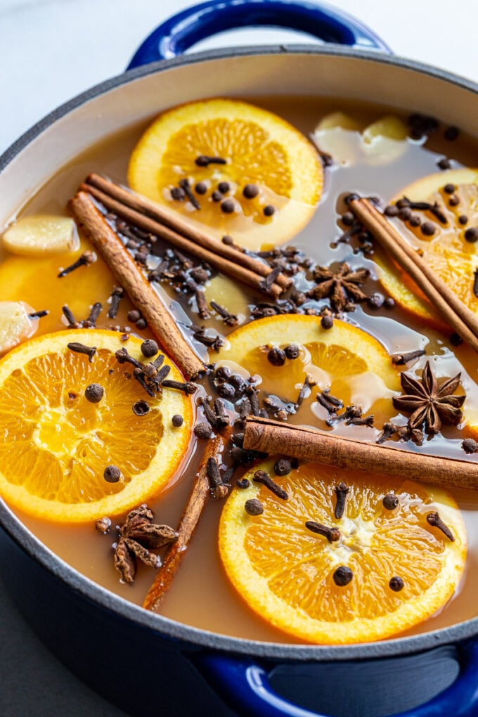 Mulling apple cider in a large pot with spices and orange slices.