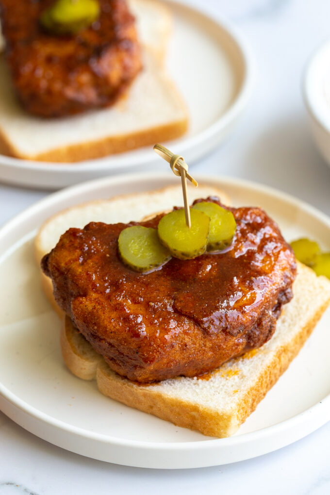 bread and fried piece of tofu covered in Nashville hot chicken sauce. It's sitting on top of slices of white bread and topped with slices of pickel