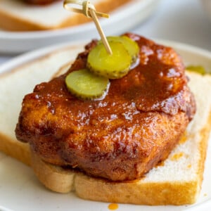 bread and fried piece of tofu covered in Nashville hot chicken sauce. It's sitting on top of slices of white bread and topped with slices of pickel