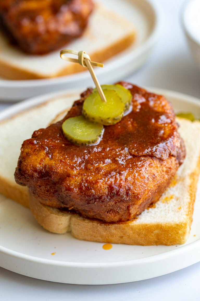 bread and fried piece of tofu covered in Nashville hot chicken sauce. It's sitting on top of slices of white bread and topped with slices of pickel