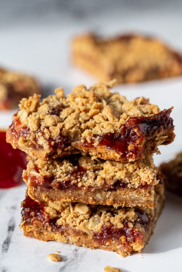 peanut butter and jelly crumble bars stacked on top of each other with more in the background