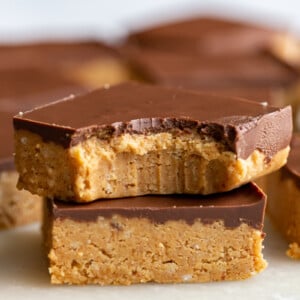 2 chocolate peanut butter bars stacked on top of each other. the top bar has a bite out of it and there are more bars in the background