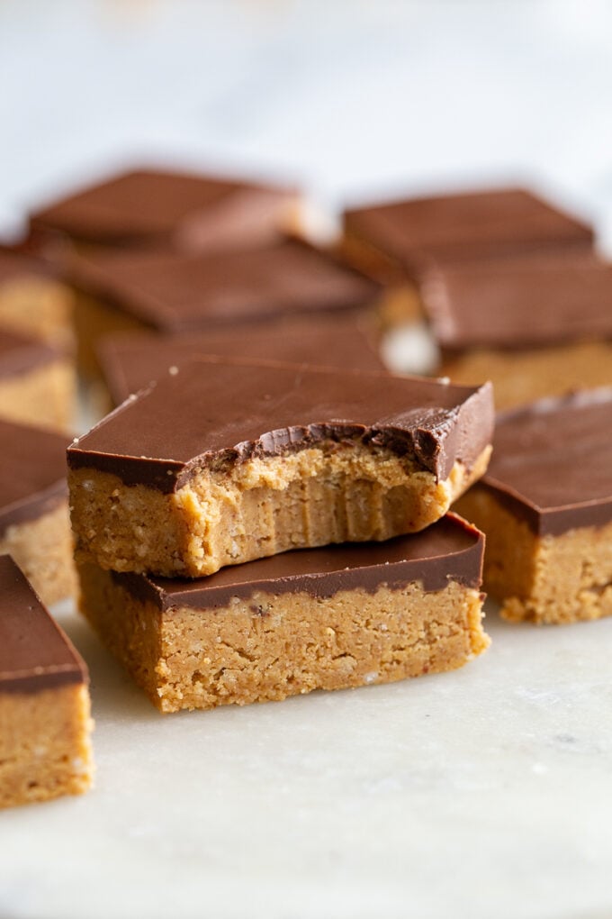 2 chocolate peanut butter bars stacked on top of each other. the top bar has a bite out of it and there are more bars in the background