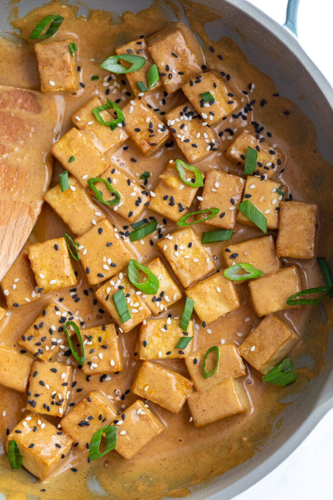 Stirring tofu in a pan with peanut sauce.