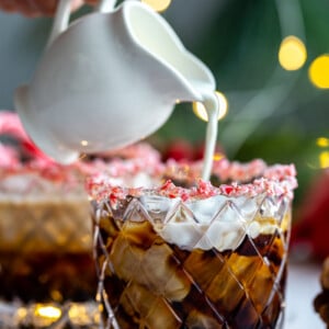 white russian in a whiskey glass with crushed peppermint around teh rim and twinkle lights in the background