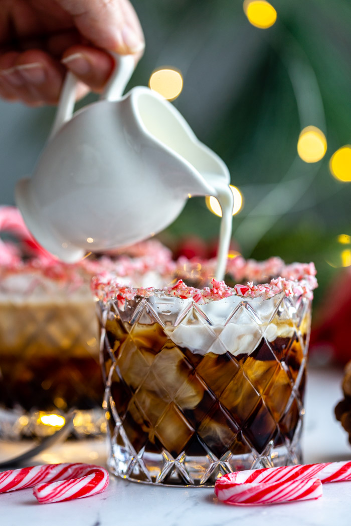 white russian in a whiskey glass with crushed peppermint around teh rim and twinkle lights in the background