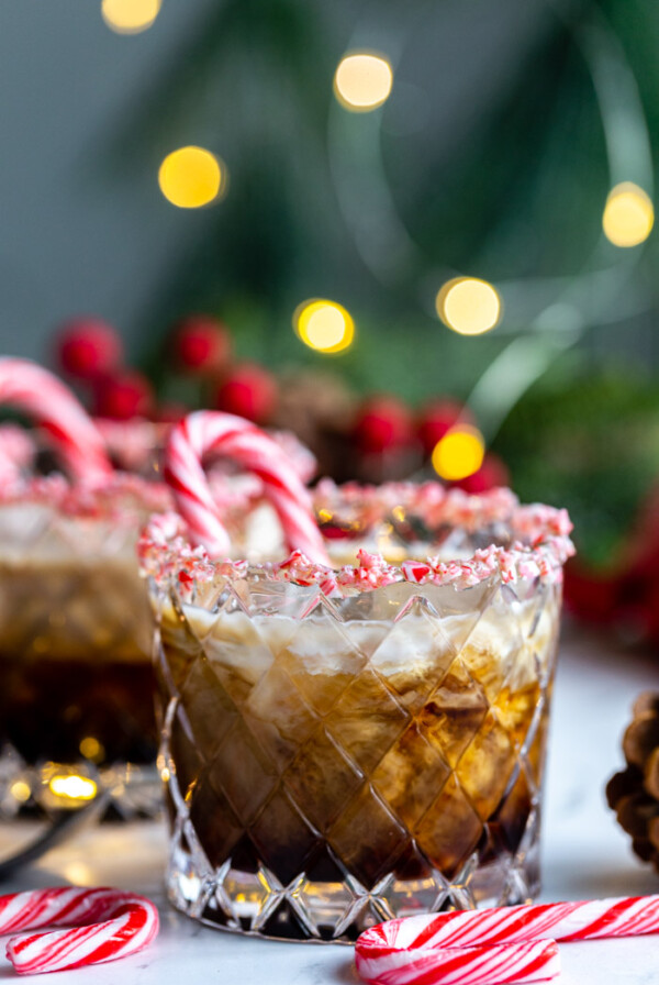 white russian in a whiskey glass with crushed peppermint around teh rim and twinkle lights in the background