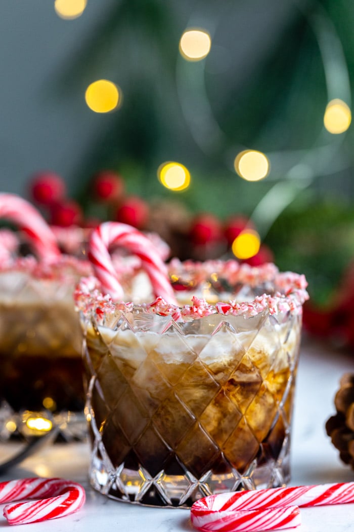 white russian in a whiskey glass with crushed peppermint around teh rim and twinkle lights in the background