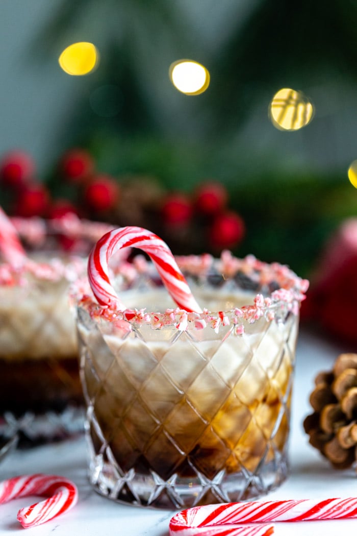 white russian in a whiskey glass with crushed peppermint around teh rim and twinkle lights in the background