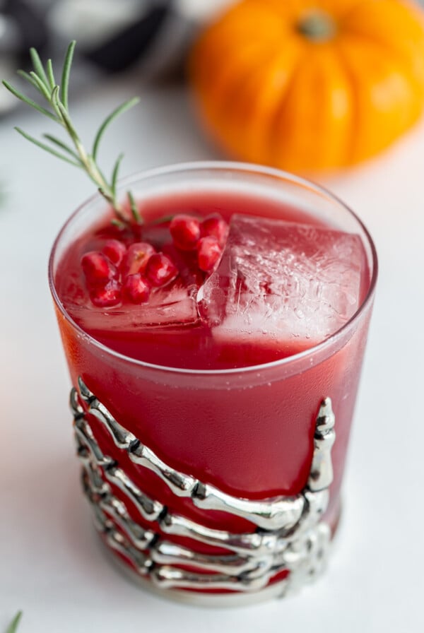 red pomegranate cocktail in a glass cup that's got a metal skeleton hand attached to it as a decoration