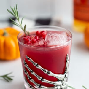 red pomegranate cocktail in a glass cup that's got a metal skeleton hand attached to it as a decoration