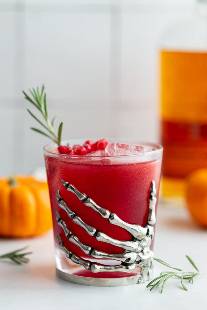 red pomegranate cocktail in a glass cup that's got a metal skeleton hand attached to it as a decoration