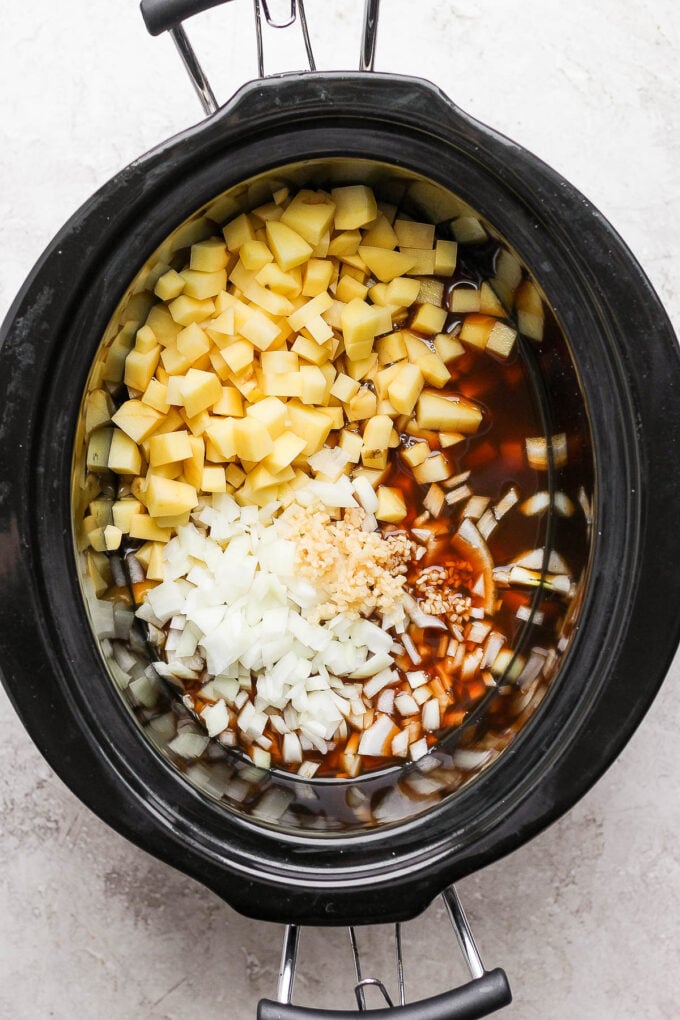 Adding potatoes and onions to crockpot for potato soup.