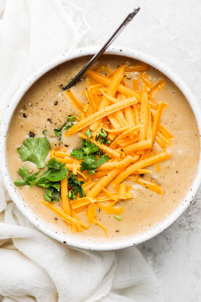 Crockpot potato soup served in a white bowl with cheddar cheese.