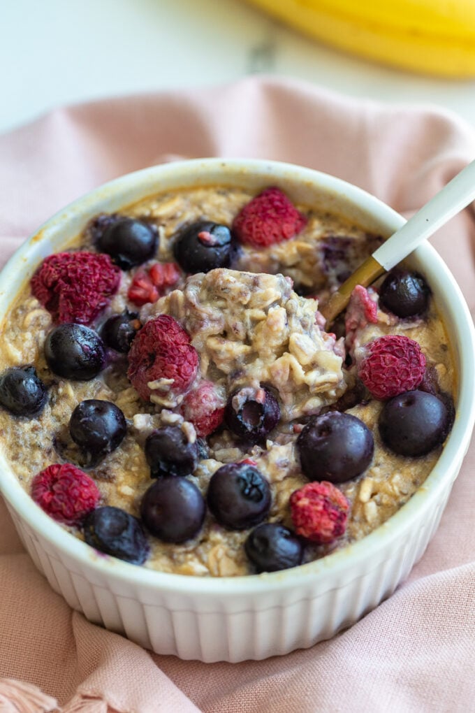 single serve baked protein oats in a ramekin and topped with fruit. A bite has been taken out of the center