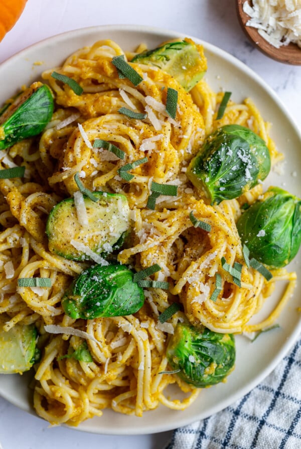 large plate of spaghetti covered in pumpkin sauce with halved brussels sprouts on top