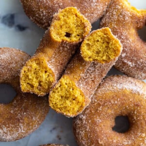 cinnamon sugar baked pumpkin donuts on a tray. 1 donut is cut in half so you can see the inside