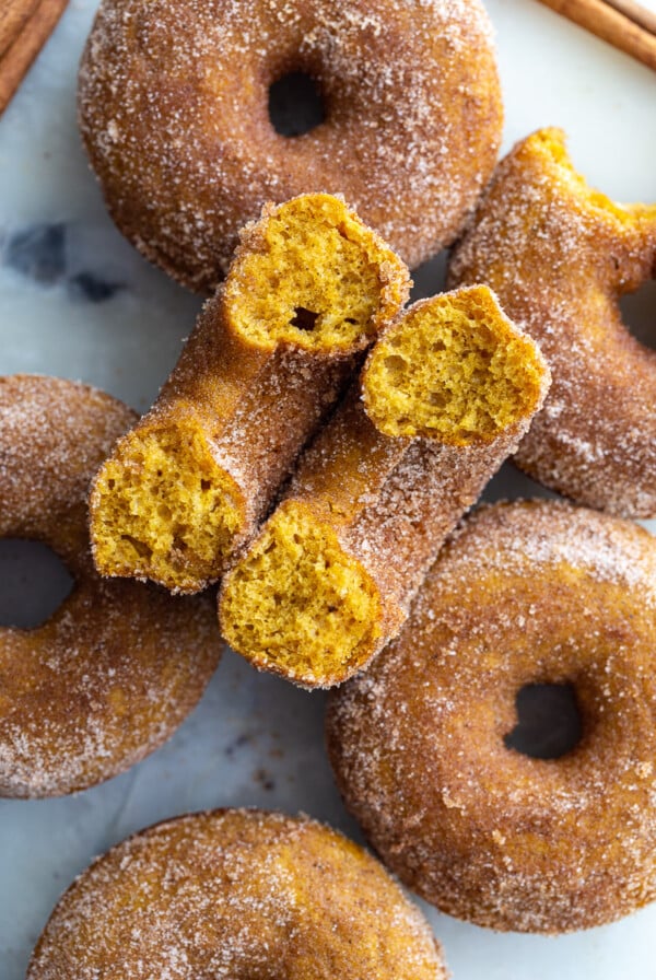 cinnamon sugar baked pumpkin donuts on a tray. 1 donut is cut in half so you can see the inside