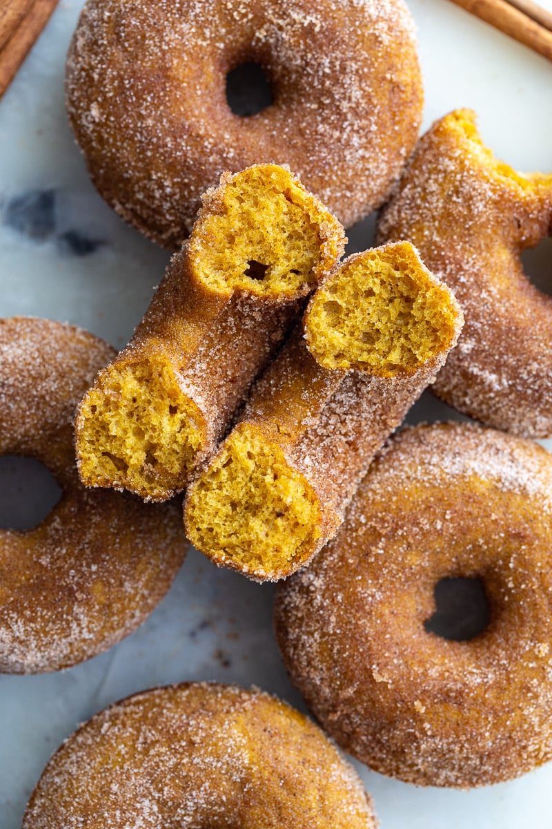 cinnamon sugar baked pumpkin donuts on a tray. 1 donut is cut in half so you can see the inside