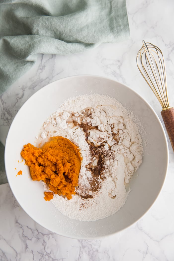 ingredients to make pumpkin donuts in a large white bowl before being whisked