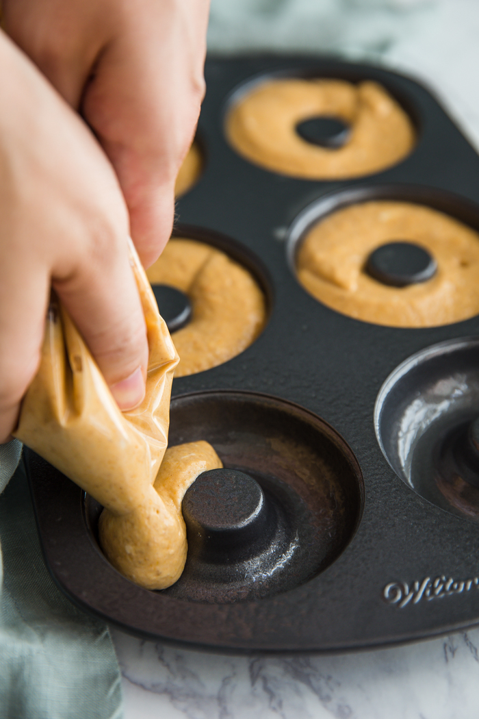 pumpkin donut batter being piped into a donut pan